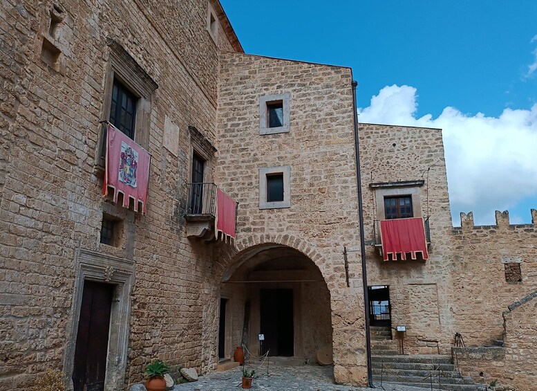 A stone building with a central archway, red cloths hanging from balconies, and a clear blue sky. 5