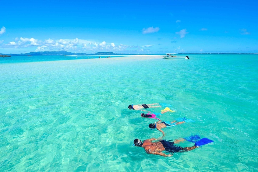 Snorkelers floating on the ocean with a boat and a distant island in the background. 1