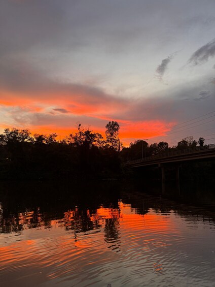 A sunset over a river with reflections, a bridge, and trees silhouetted against the sky. 2