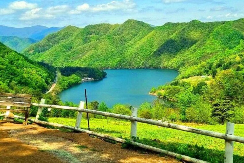 A lake surrounded by lush green hills, a wooden fence, and a clear sky. 3