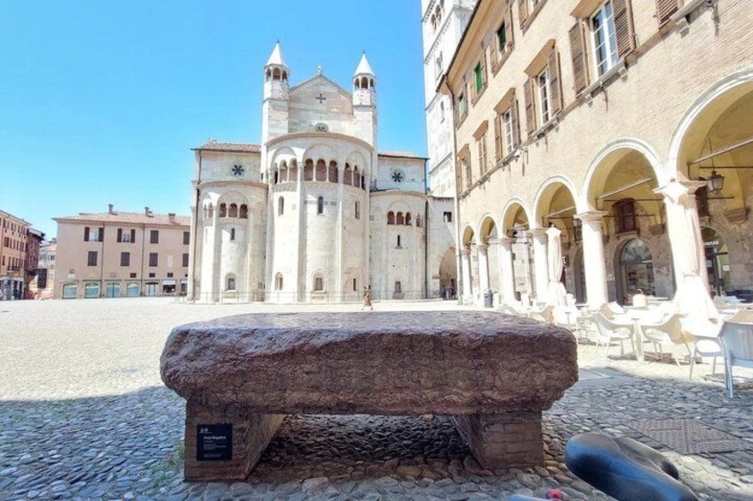 A historic building with a clock tower, a stone bench, and an open plaza with tables and chairs. 5