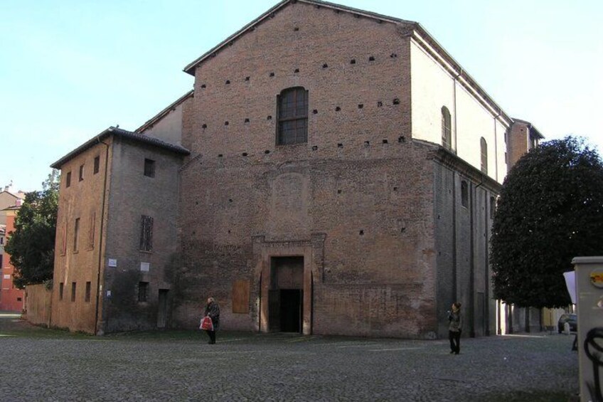 A historic building with a large arched entrance, a brick facade, and a courtyard. 1