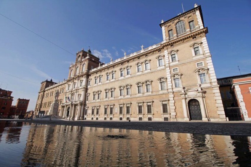 A historic building with classical architecture, a reflective water surface in front, and a clear blue sky. 4