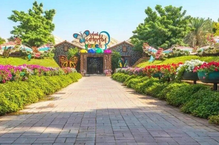 A pathway leading to a building with a butterfly sign, surrounded by colorful flower beds. 2