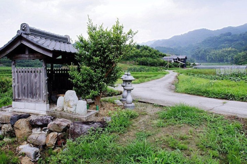 A traditional Japanese structure, a stone lantern, and a rural path leading to a house in a mountainous area. 1