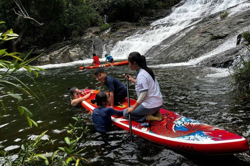 People on a red paddleboard in a river surrounded by rocks and greenery. 3