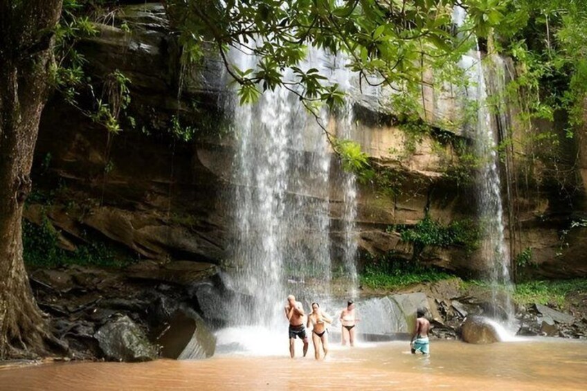 A waterfall in a forested area with people enjoying the water. 3