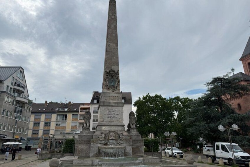 A tall obelisk monument with inscriptions, surrounded by buildings and trees. 4