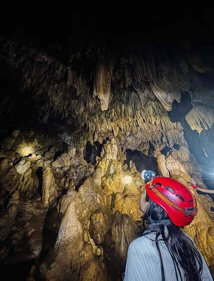 A person wearing a red helmet exploring a cave with stalactites. 4
