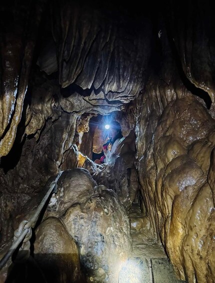 A cave with stalactites and stalagmites, a person with a headlamp, and a rope for safety. 5