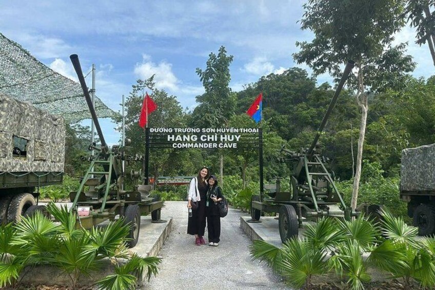 A military vehicle, a sign with flags, and a person standing in front of the vehicle. 2