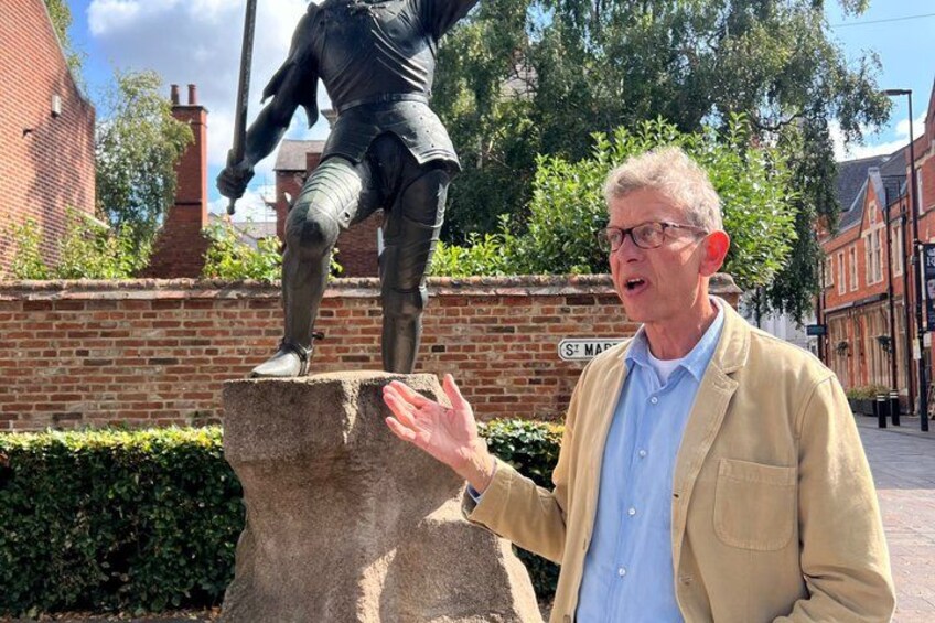 A person standing next to a statue of a knight on a stone pedestal. 2