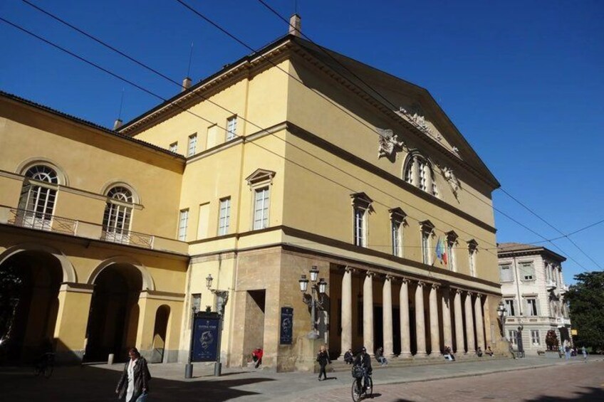 A yellow building with columns, arched doorways, and flags. 5