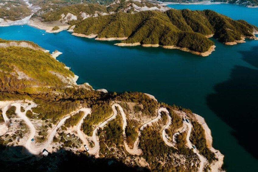 An aerial view of a coastal area with winding roads, dense forests, and a large body of water. 1