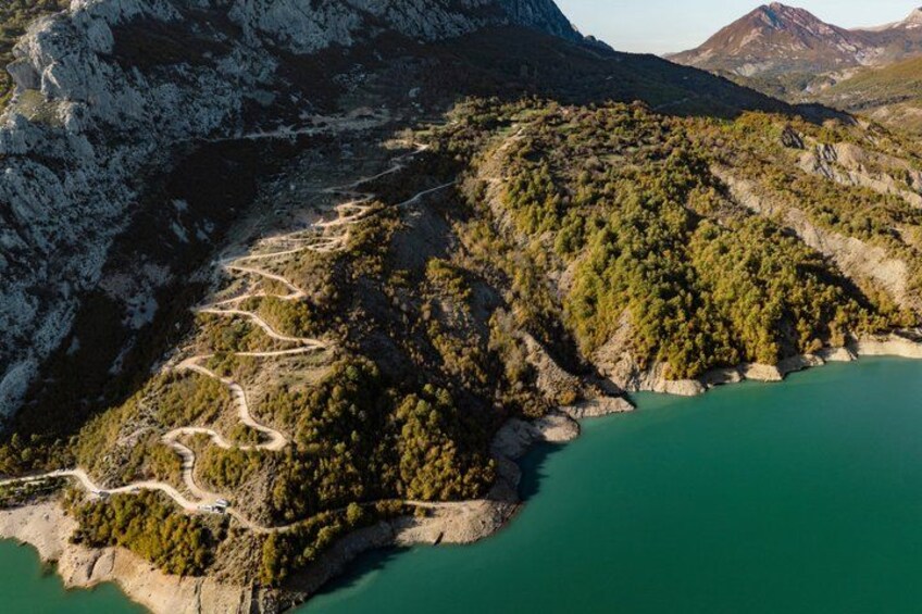 A mountainous landscape with a winding road, a lake, and dense forest. 5