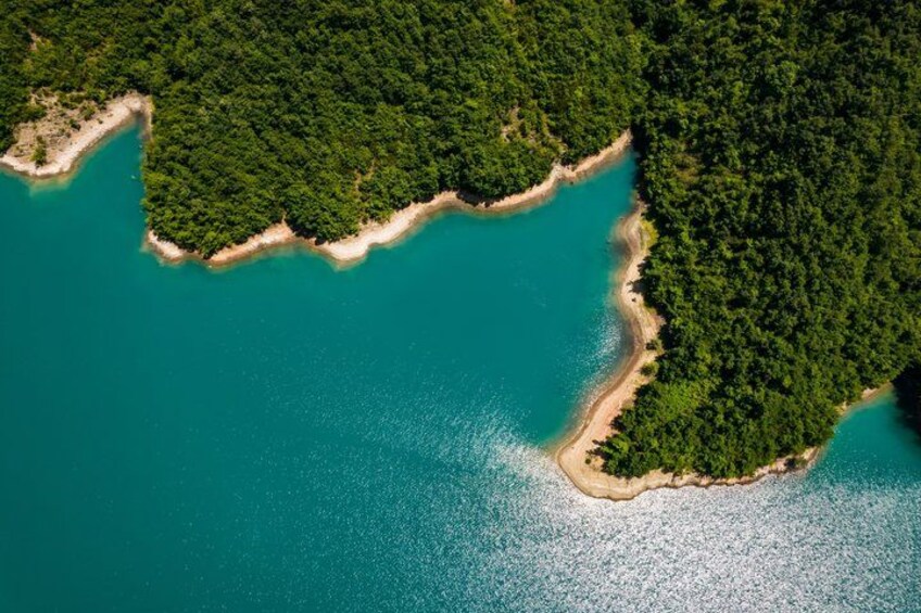 An aerial view of a coastal area with dense green vegetation and a clear turquoise sea. 3
