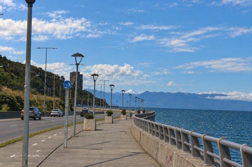 A coastal road with a pedestrian walkway, street lamps, and a view of the sea and mountains. 5