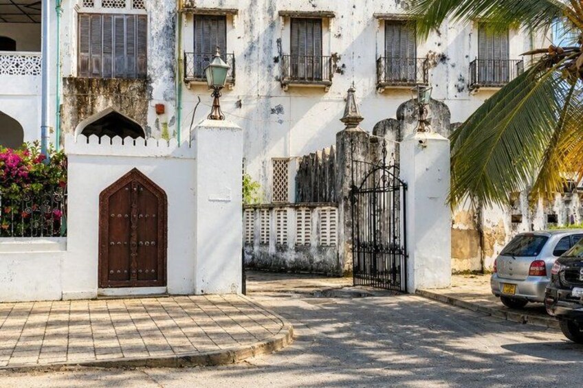 A white building with a brown door, a black gate, and a palm tree. 4