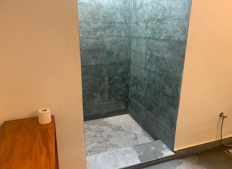 A bathroom with dark green tiles, a wooden stool, and a roll of toilet paper. 2