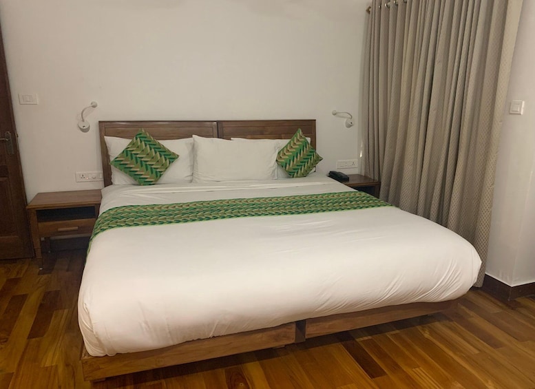 A neatly made bed with white linens and green patterned pillows, a wooden headboard, and a wooden nightstand with a phone. 4
