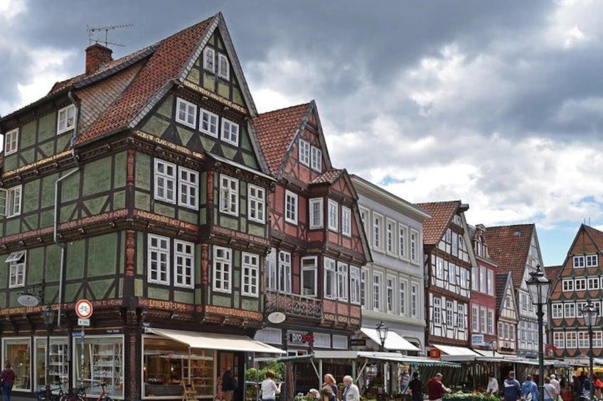 A traditional European town with half-timbered houses, a market area with people, and a cloudy sky. 4