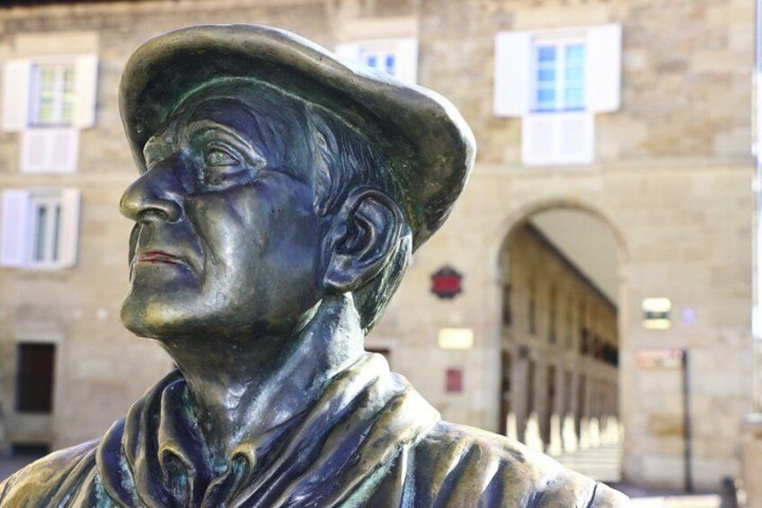 A bronze statue of a man with a hat, set against a stone building with arched windows. 4