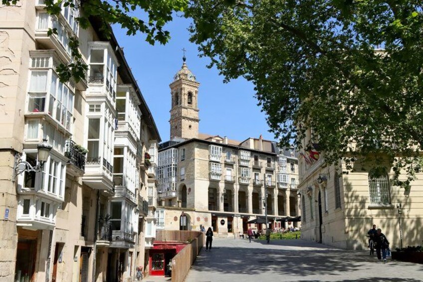 A historic square with buildings, a tower, and a tree. 5