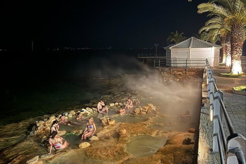 People sitting on rocks by the water at night. 1