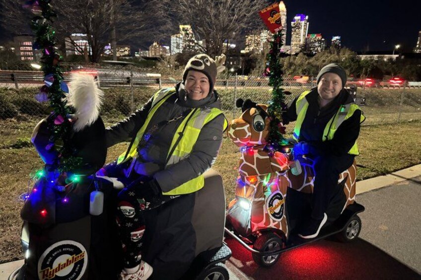 Two people on electric scooters decorated with Christmas lights and a Santa hat. 3