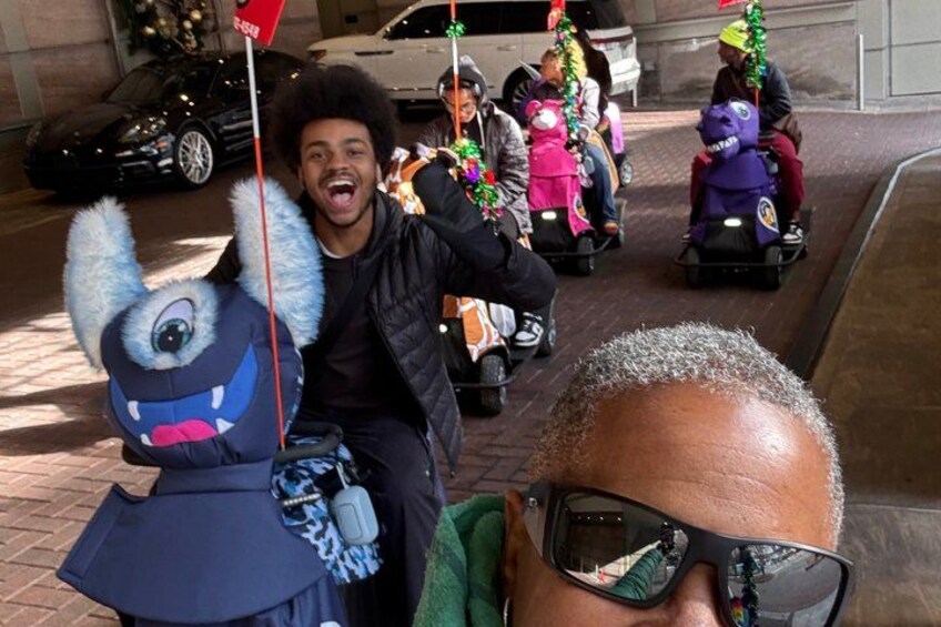 A person on a ride-on toy with a blue furry head, a car parked in the background, and a building facade. 5