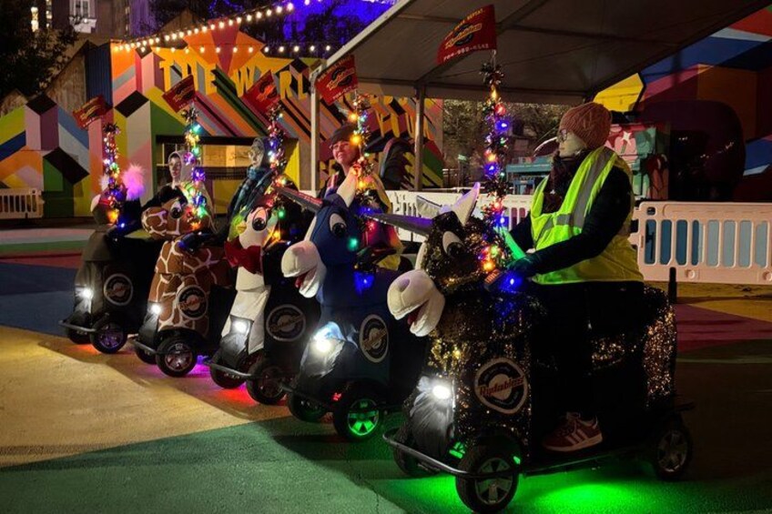 A nighttime street scene with a row of decorated vehicles and a person in a safety vest. 1