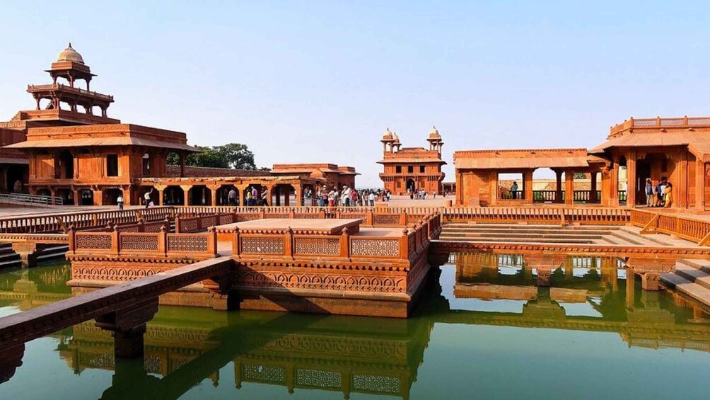 A historic architectural complex with ornate structures, a reflective water body, and a bridge. 2