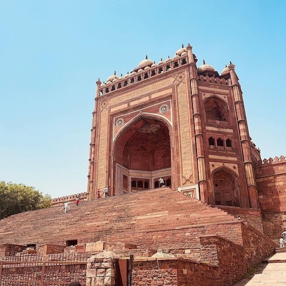 A large, ornate red sandstone structure with a large archway and multiple domes. 1