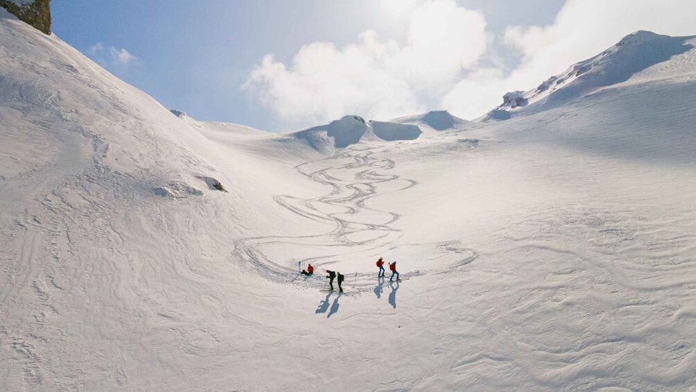 A snowy landscape with a winding path and three people in red jackets. 1
