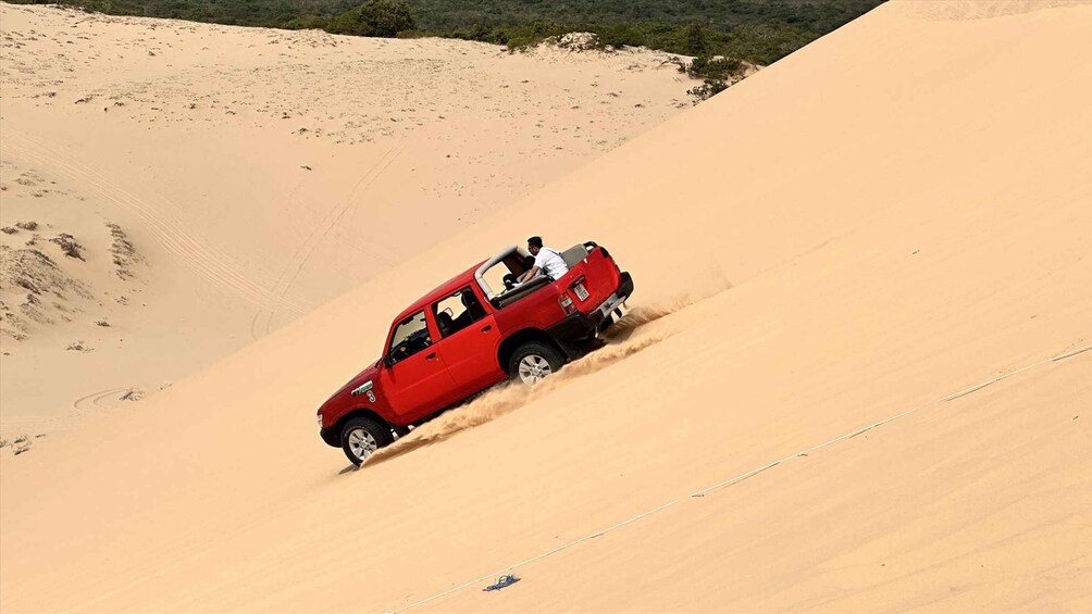 Un véhicule tout-terrain rouge traverse une dune de sable. 1