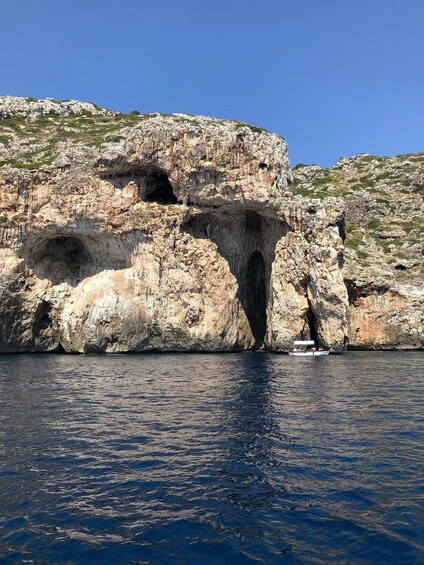 Una costa rocosa con la entrada de una cueva y un pequeño bote en el agua. 2