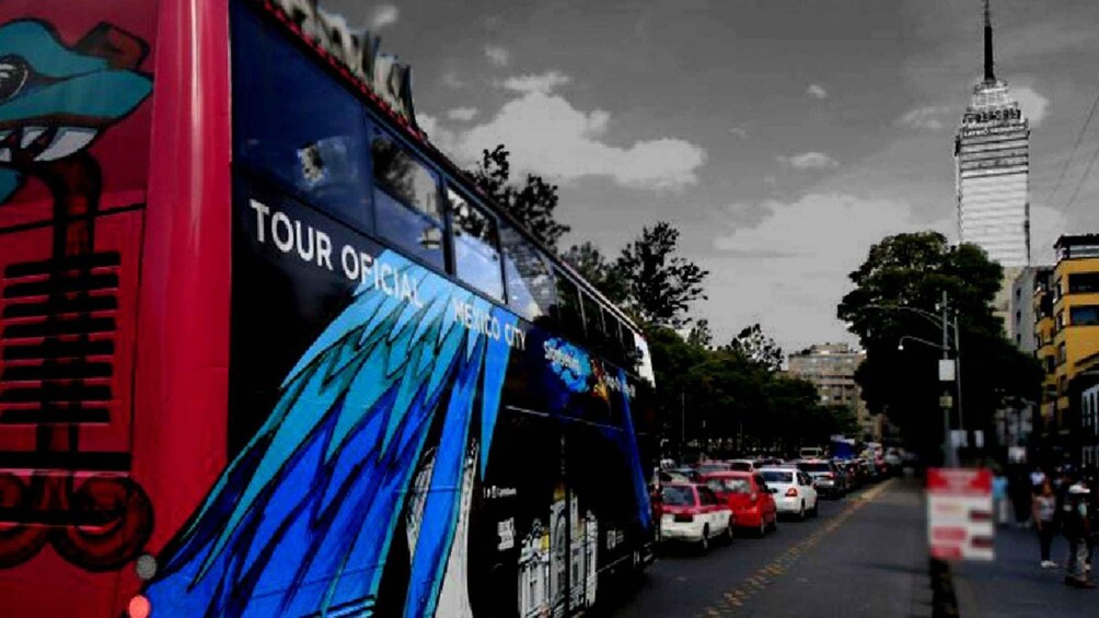 Un autobús de dos pisos con la leyenda 'TOUR DE LA CIUDAD DE MÉXICO', estacionado en una calle con automóviles y edificios al fondo. 3