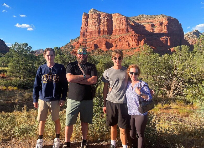 Four people standing in a natural landscape with red rock formations in the background. 3