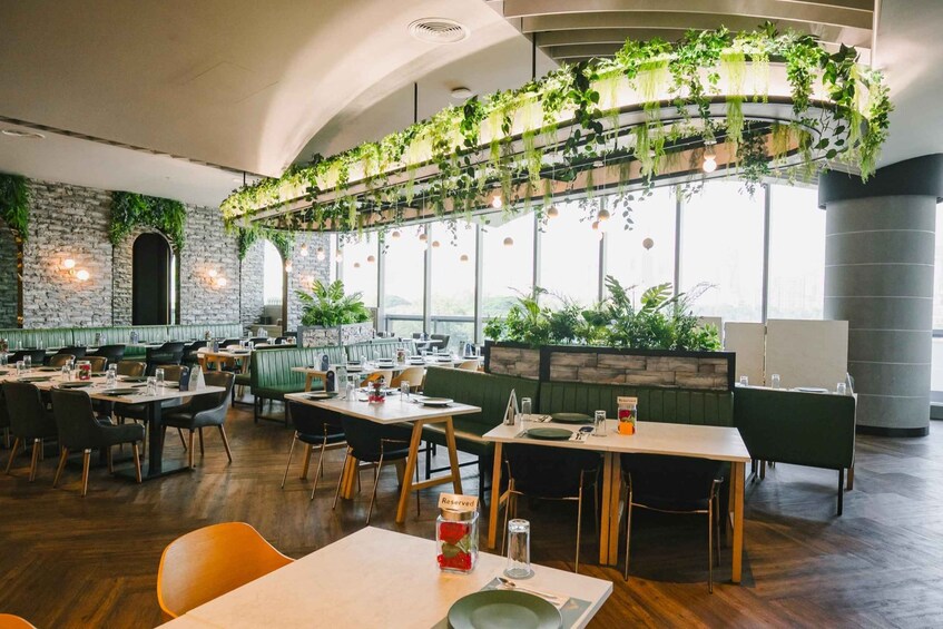 En restaurantindretning med træborde, grønne polstrede bænke og hængende planter. 5