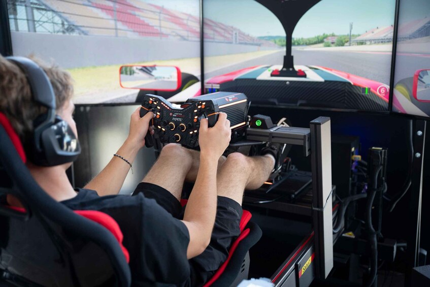 A person seated in a racing simulator cockpit, holding a racing steering wheel controller. 1