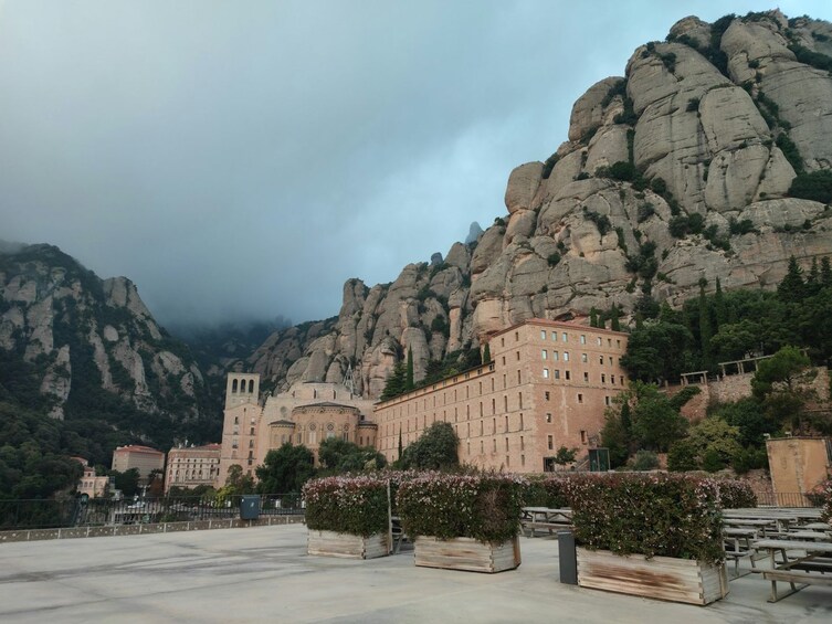 A historic building with classical architecture, surrounded by rocky mountains and a cloudy sky. 1