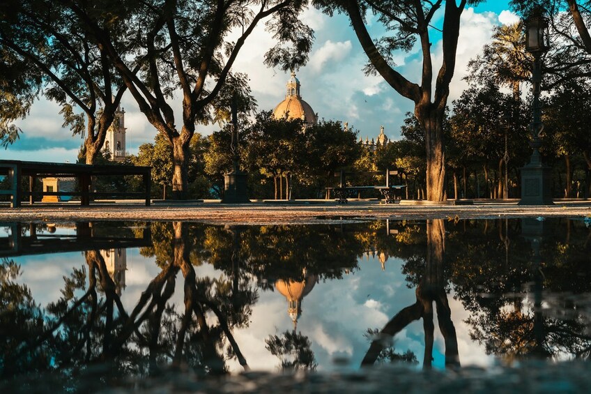 Ein Park mit einem großen, spiegelnden Teich, Bäumen und einer markanten Kuppel im Hintergrund. 3
