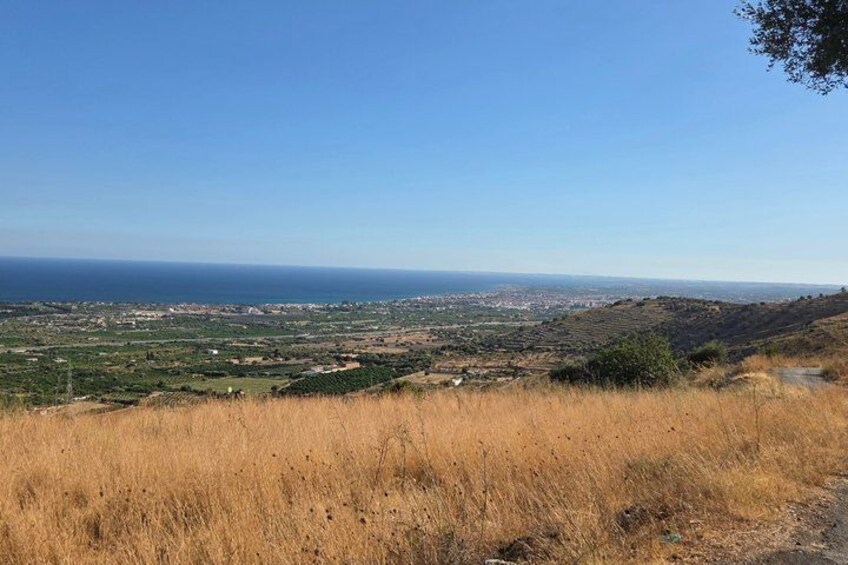 Un paisaje costero con cielo despejado, un primer plano de hierba y vista al mar y edificios distantes. 3