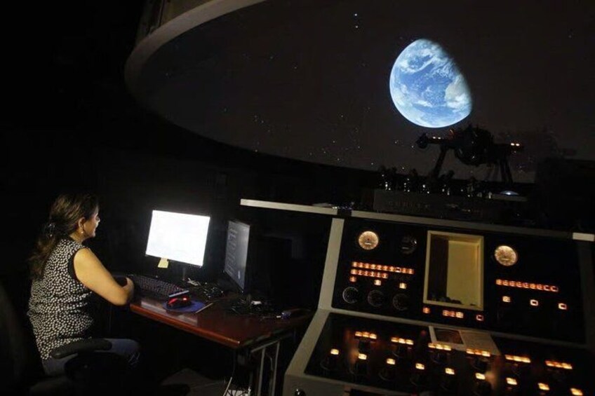 A person at a control panel with a large screen displaying a planet. 5