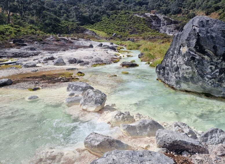 A clear river flowing through a rocky landscape with large boulders and a small structure on a hill. 4