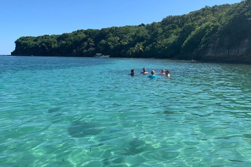 Clear turquoise water, a group of people swimming, and a forested cliff in the background. 3