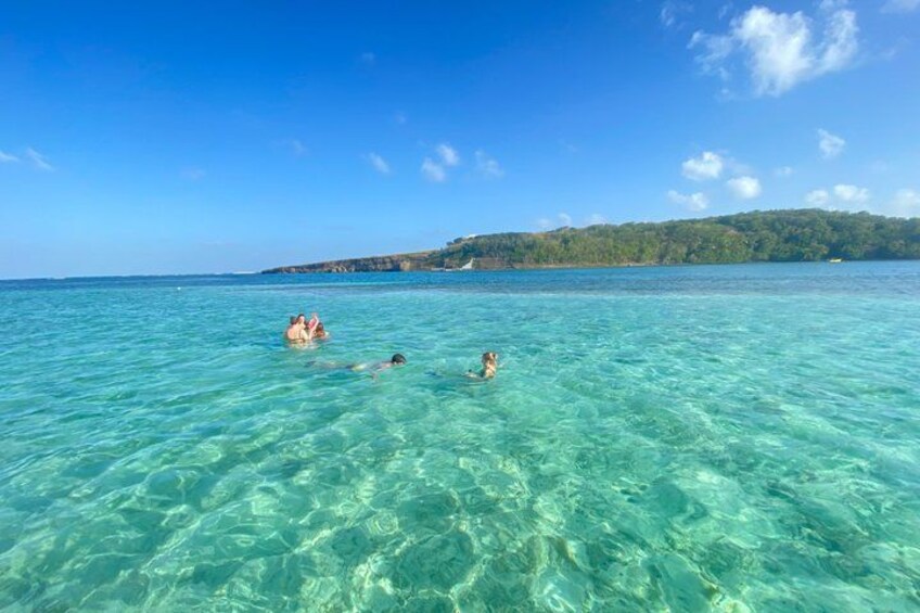 Clear turquoise water, people swimming, and a distant shoreline with trees. 1