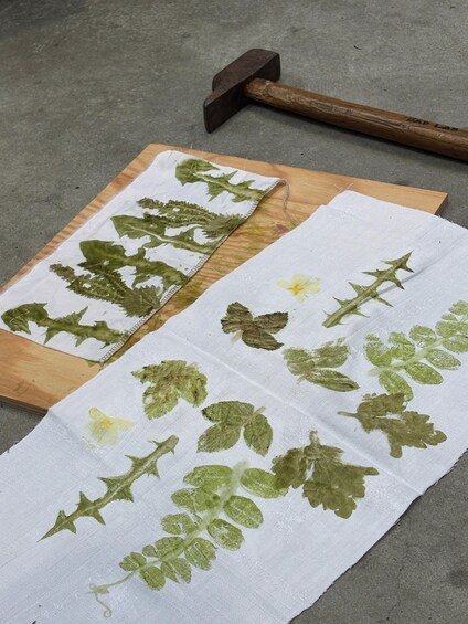 A wooden surface with a white cloth featuring green leaf patterns and a hammer. 2