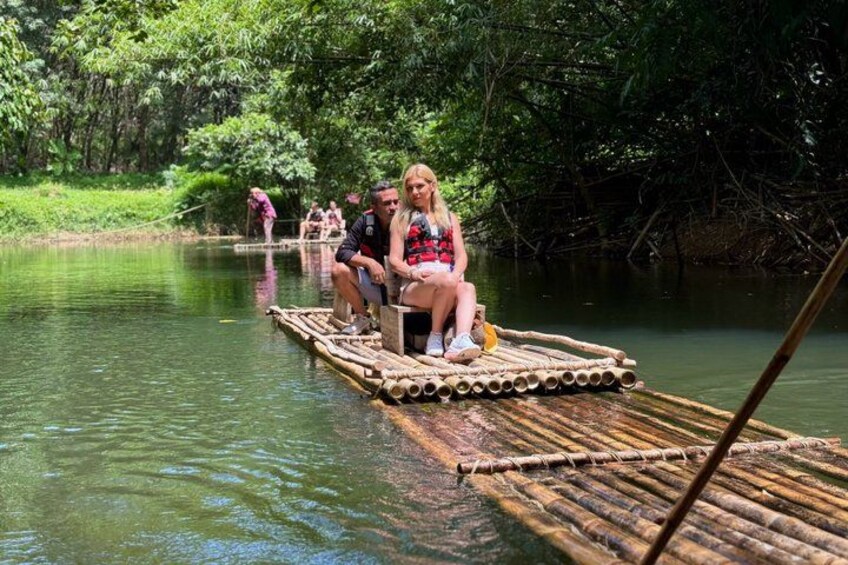 A bamboo raft with people sitting on it in a river surrounded by greenery. 1