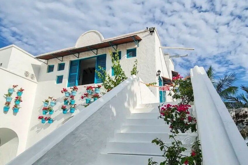A white building with blue shutters, a staircase, and potted plants. 3